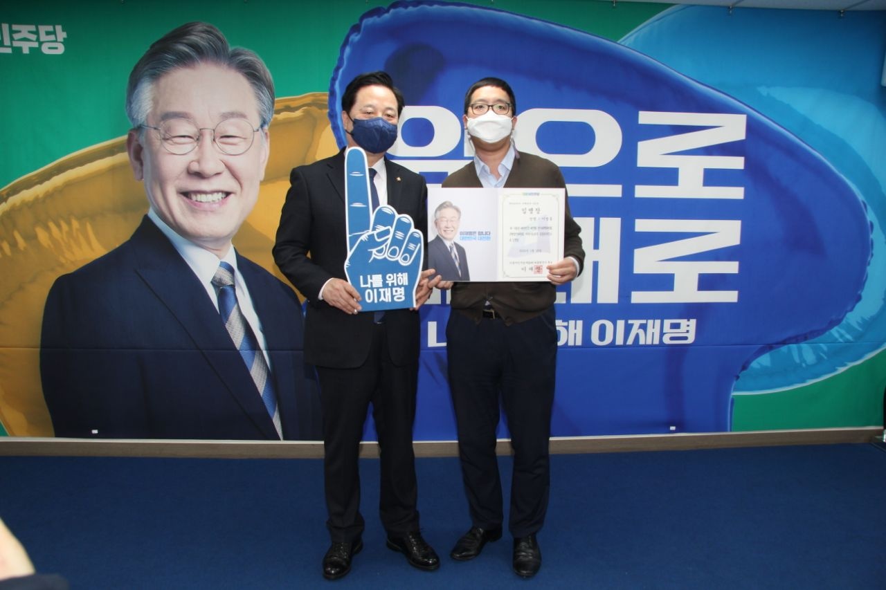 YoungJong Lee (right) with a colleague in front of a banner featuring the presidential candidate.