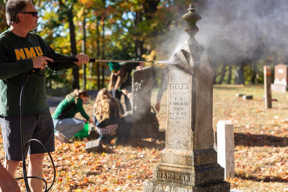 NMU President Chris Olsen powerwashes a gravestone after scrubbing moss and dirt from the marker.