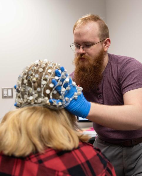 Graduate student Elijah Nieman places the current 64-electrode EEG on a research subject. The new integrated system will feature two high-density EEGs with 256 electrodes each.