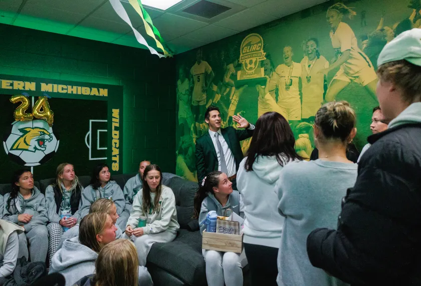 Sandoval (center) points to the updated mural featuring photos from last year's GLIAC Championship during an open house for the renovated locker room earlier this season.