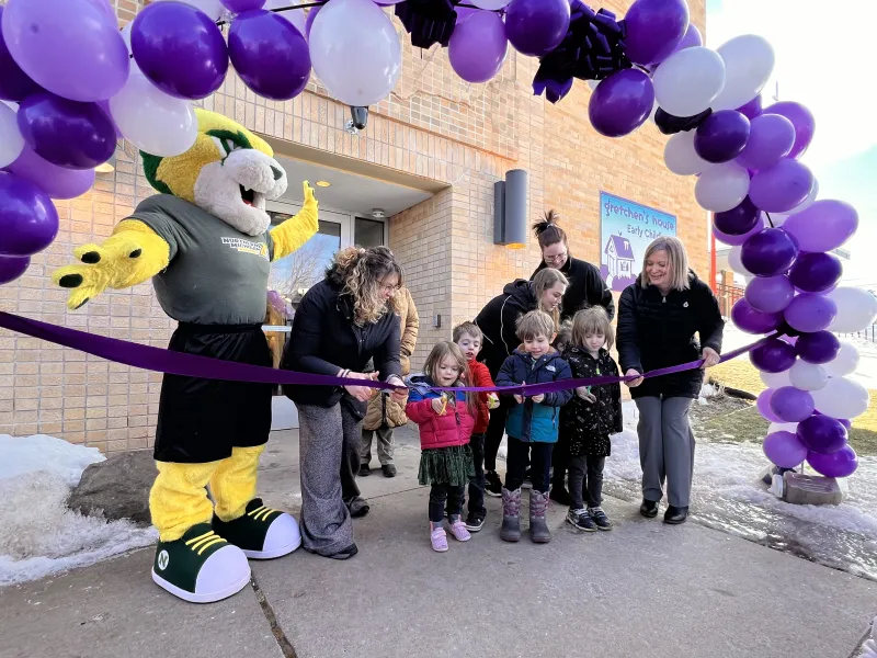 Children preparing to cut the ribbon at Gretchen's House, with Wildcat Willy and others looking on.