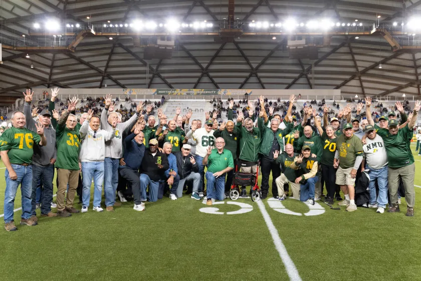 The 1975 team members hold up four fingers as a tribute to the late coach Buck Nystrom's fourth-quarter program when they were honored during halftime of the Wildcats Oct. 11 game in the Superior Dome.