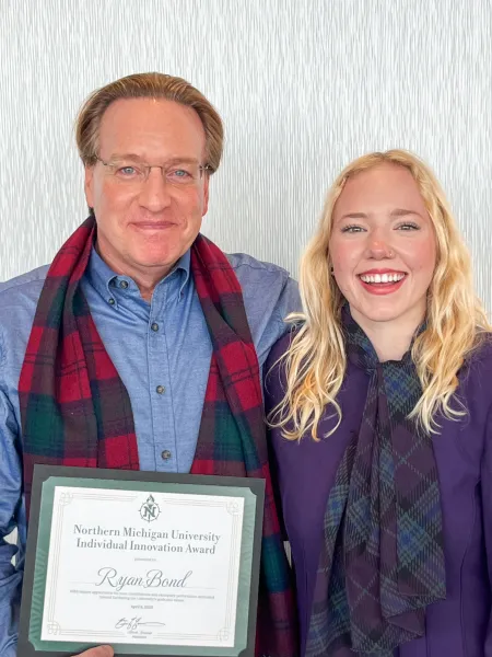 Ryan Bond with an NMU Innovation Award, standing alongside May 2025 graduate Lindsey Locke. He introduced her to the Congress-Bundestag Youth Exchange (CBYX) for Young Professionals program and, with the help of his mentorship, she was one of 65 Americans selected to study and work in Germany for a year.