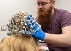 Graduate student Elijah Nieman places the current 64-electrode EEG on a research subject. The new integrated system will feature two high-density EEGs with 256 electrodes each.