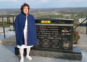 Stolze stands at the Vietnam War Memorial on top of Pine Mountain. She is dressed in the Upper Peninsula Nurses Honor Guard’s traditional white uniform, cap, and blue and red cape. (Terri Castelaz/Daily News photo)