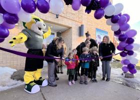 Children preparing to cut the ribbon at Gretchen's House, with Wildcat Willy and others looking on.